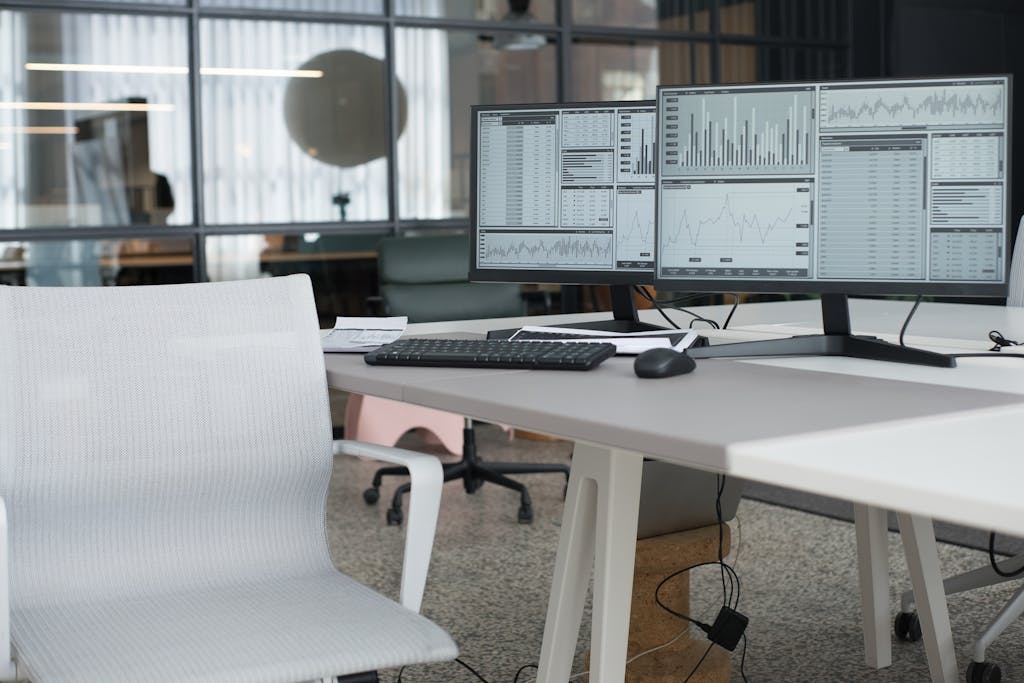 A modern office desk with dual monitors displaying data and an ergonomic chair, perfect for a productive workspace.